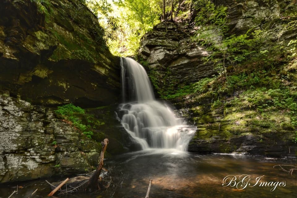 A waterfall in a forested area with moss-covered rocks and a small stream at the base.