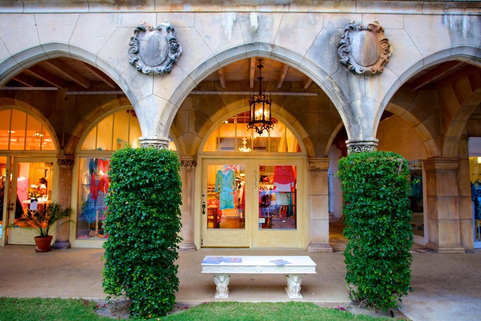 A historic building with three arches, a bench, and lush greenery.