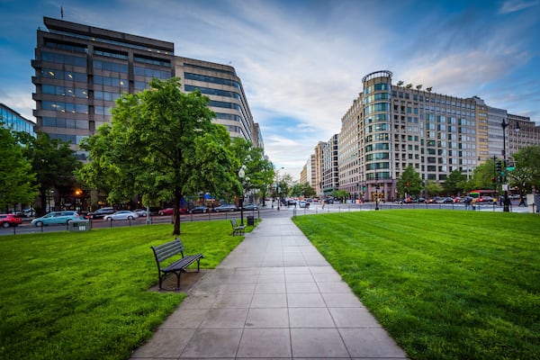 A city park with a paved walkway, benches, and green grass.