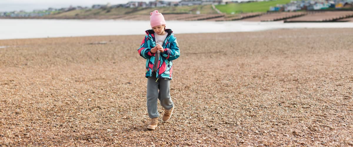 A child walking on a pebbled beach with houses in the background.