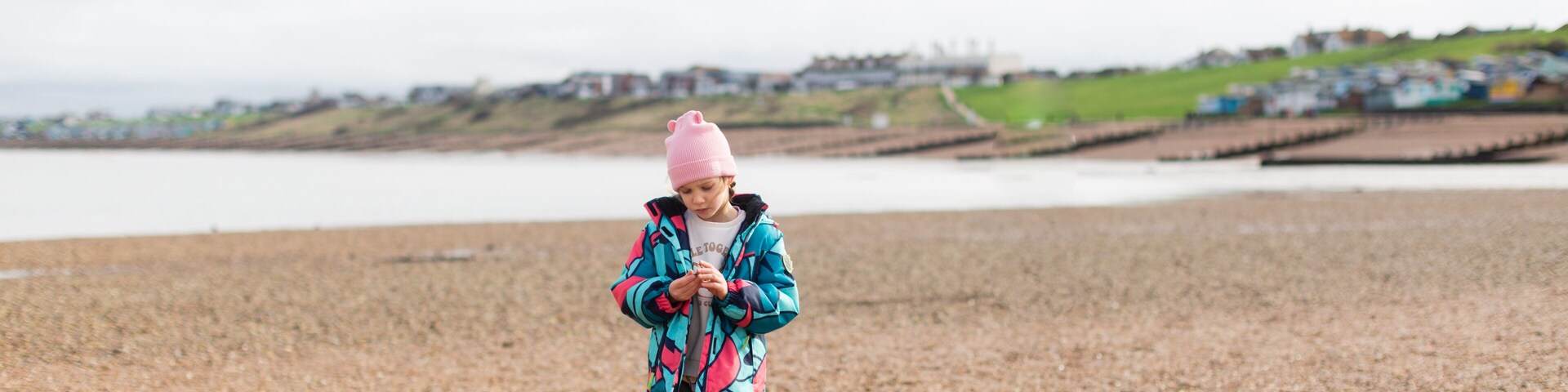 A child walking on a pebbled beach with houses in the background.