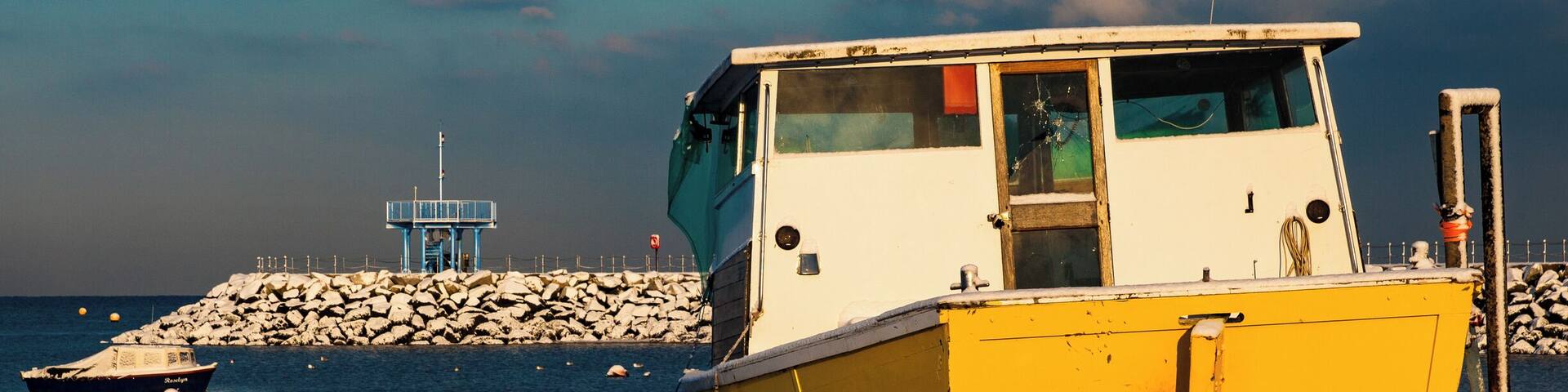 A yellow and white boat docked at a rocky pier with a lighthouse in the background.