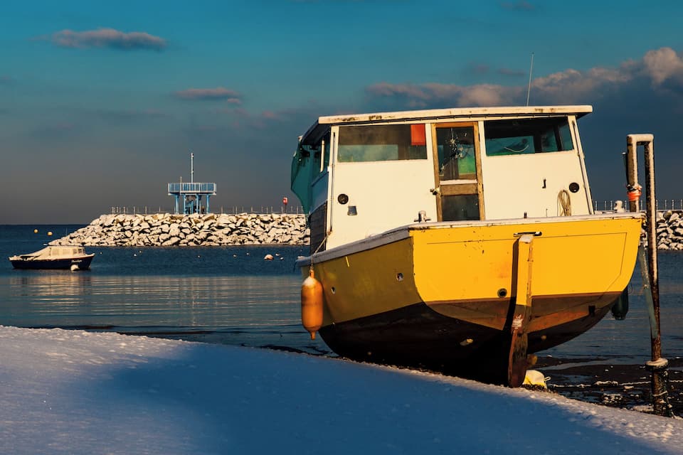 A yellow and white boat docked at a rocky pier with a lighthouse in the background.