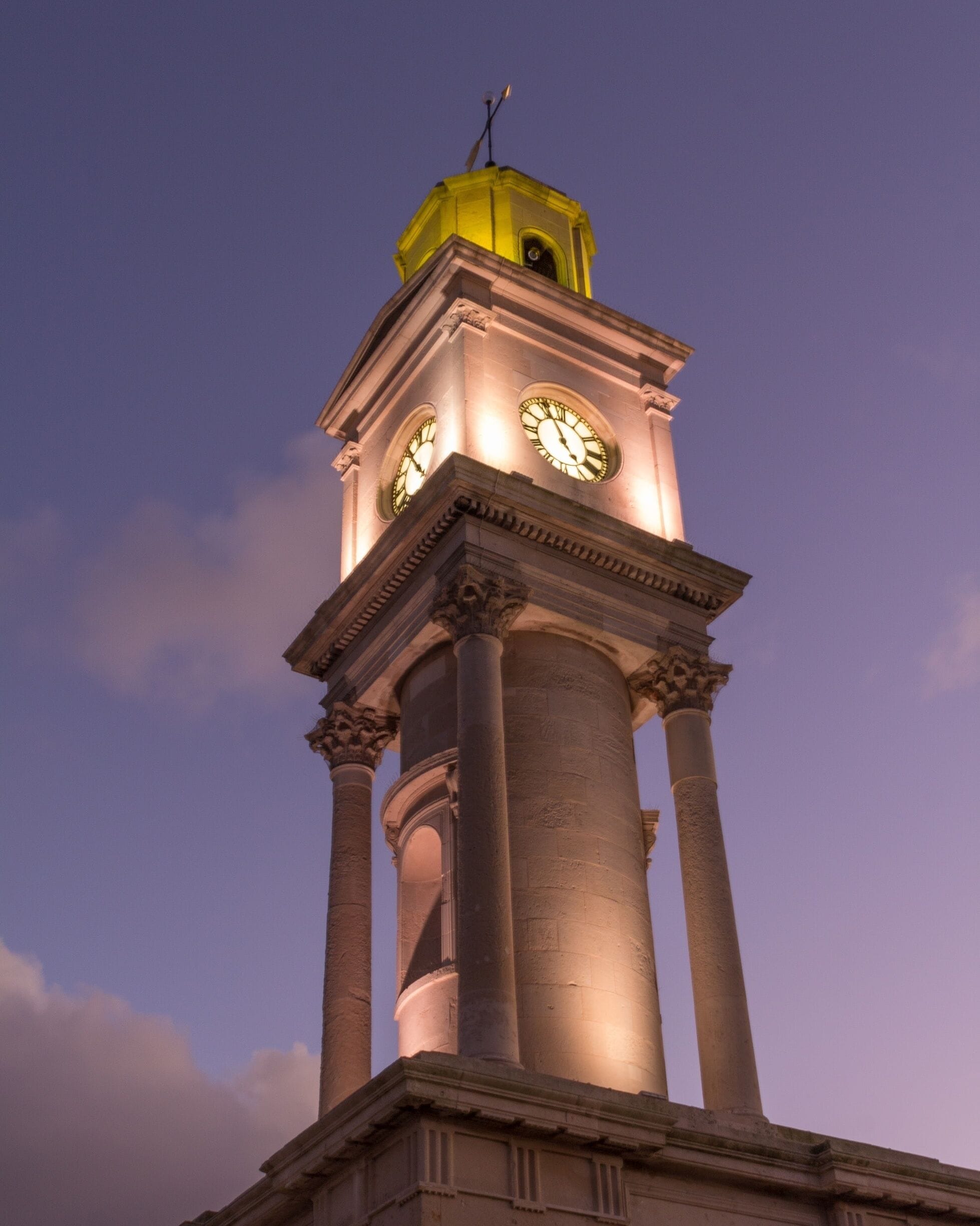 A clock tower with a yellow roof and two clocks, set against a twilight sky.