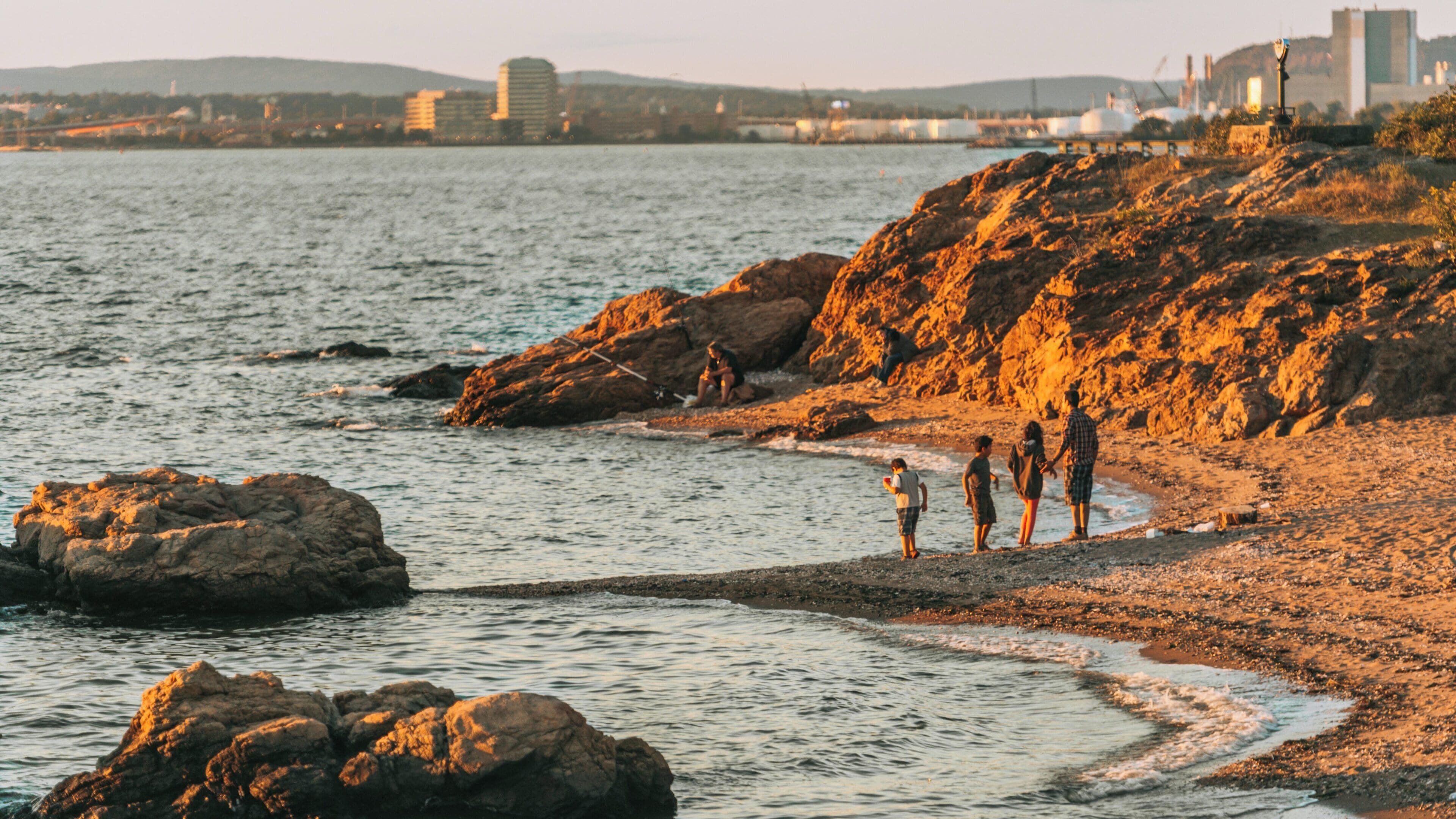 Family walks along the rocky shore at Lighthouse Point Park in East Haven, Connecticut during golden hour