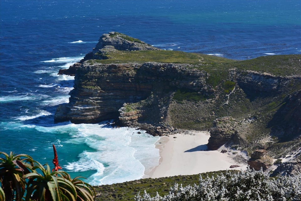 A coastal cliff with a beach and ocean waves crashing against the rocks.