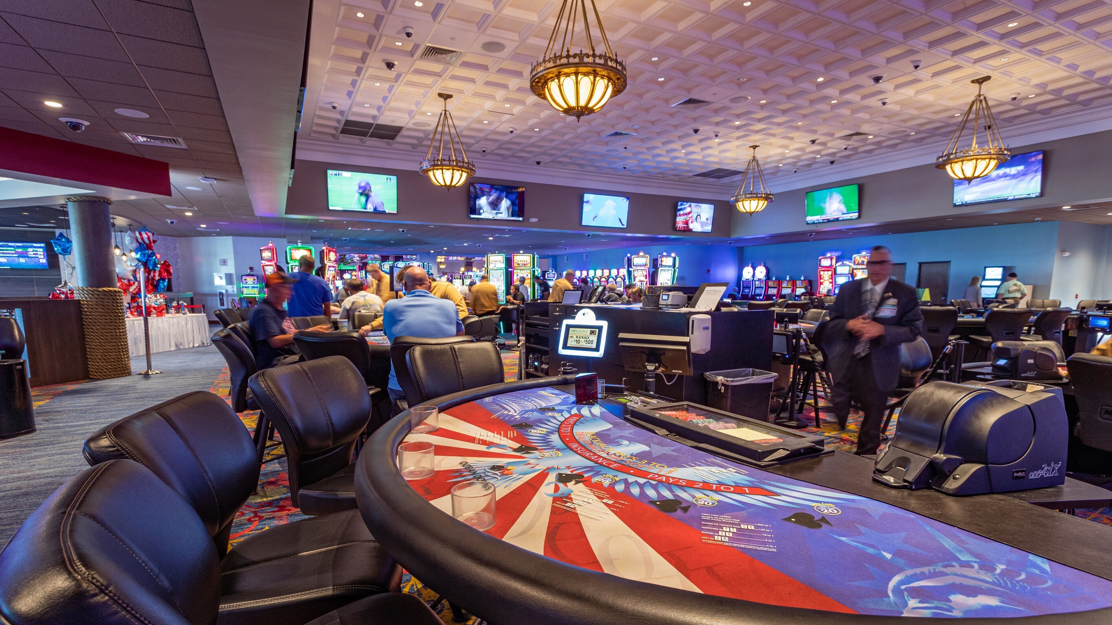 Un casino avec des tables de blackjack, des machines à sous et un grand écran diffusant un événement sportif.