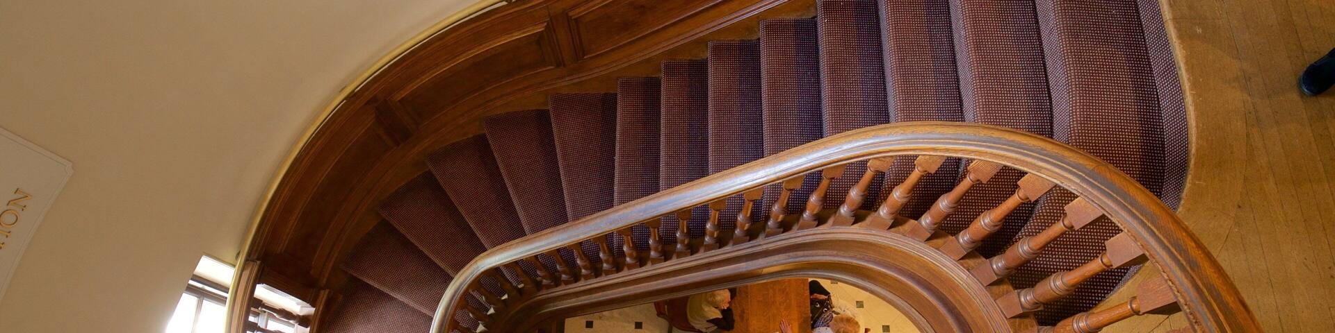 A wooden spiral staircase with a patterned carpet and a checkered floor.