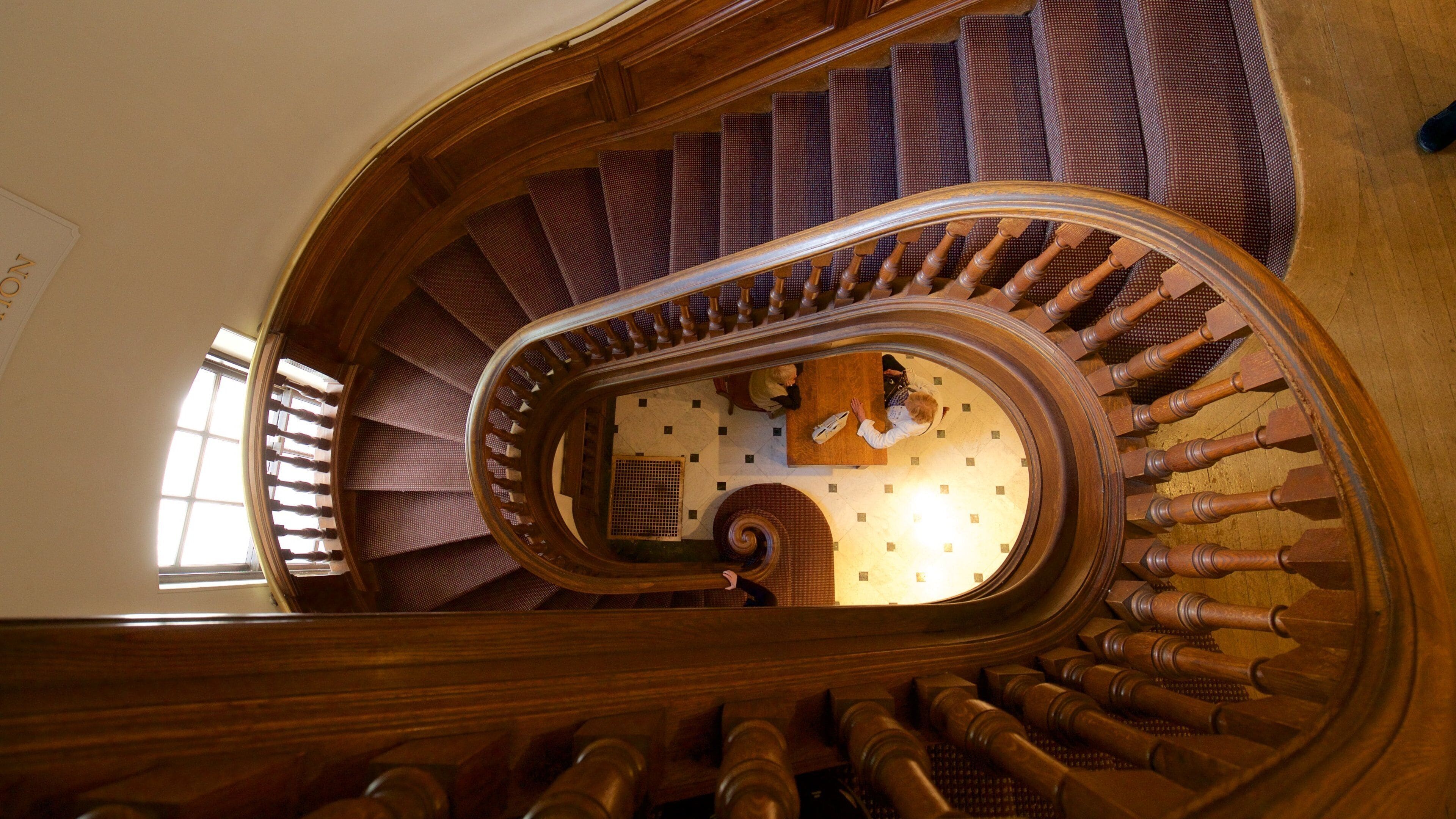A wooden spiral staircase with a patterned carpet and a checkered floor.