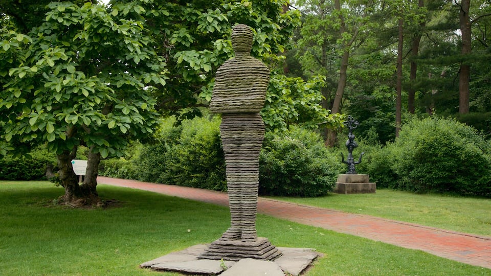 A stone sculpture of a figure in a garden with a brick path and lush greenery.