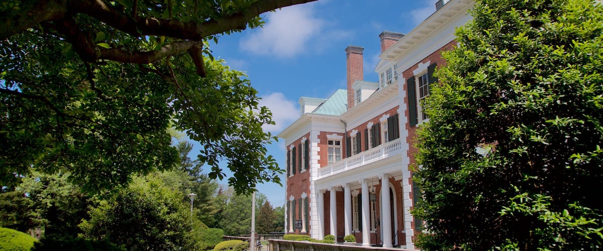 A historic brick building with a green roof, surrounded by lush greenery and a well-maintained lawn.