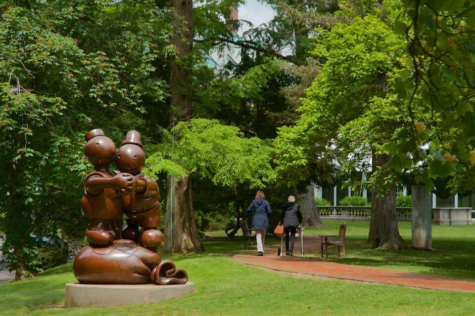 A park with a bronze sculpture of two figures, lush green trees, and a pathway.