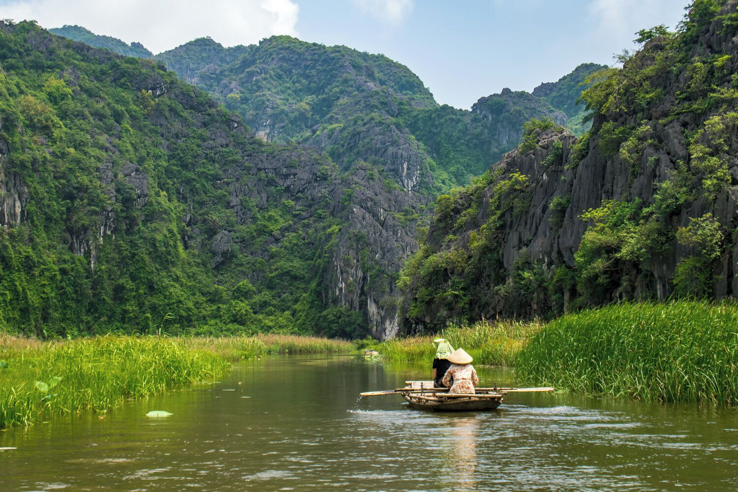 A person in a boat on a river surrounded by lush green mountains.