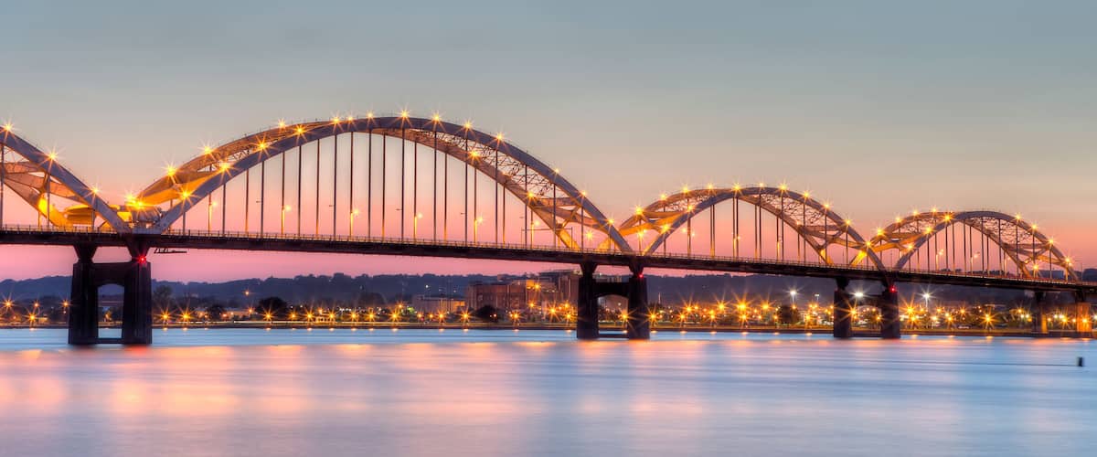 A large illuminated bridge with multiple arches over a calm river at dusk.