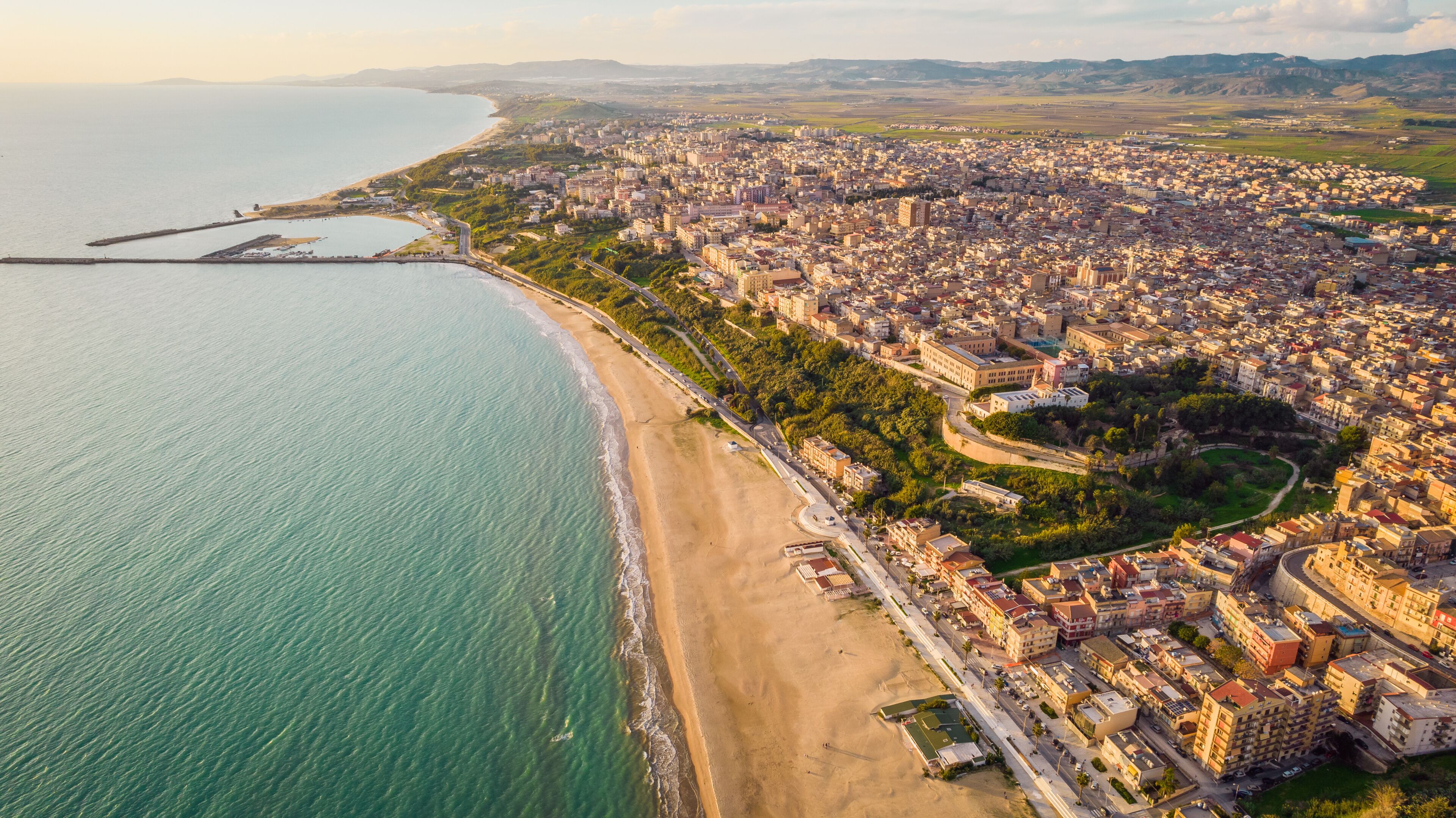 An aerial view of a coastal city with a beach, dense urban area, and distant mountains.