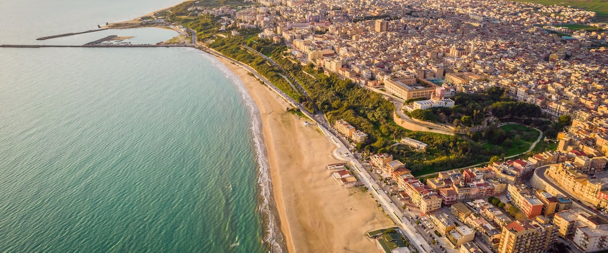 An aerial view of a coastal city with a beach, dense urban area, and distant mountains.