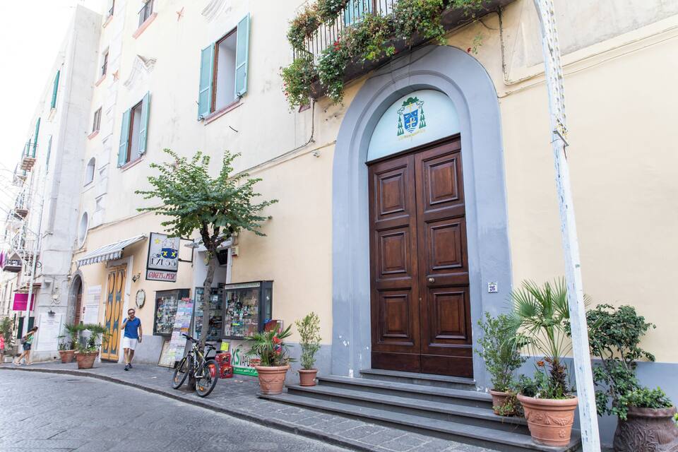 Una strada con un edificio che presenta un'ampia porta in legno, piante in vaso e una bicicletta parcheggiata all'esterno.