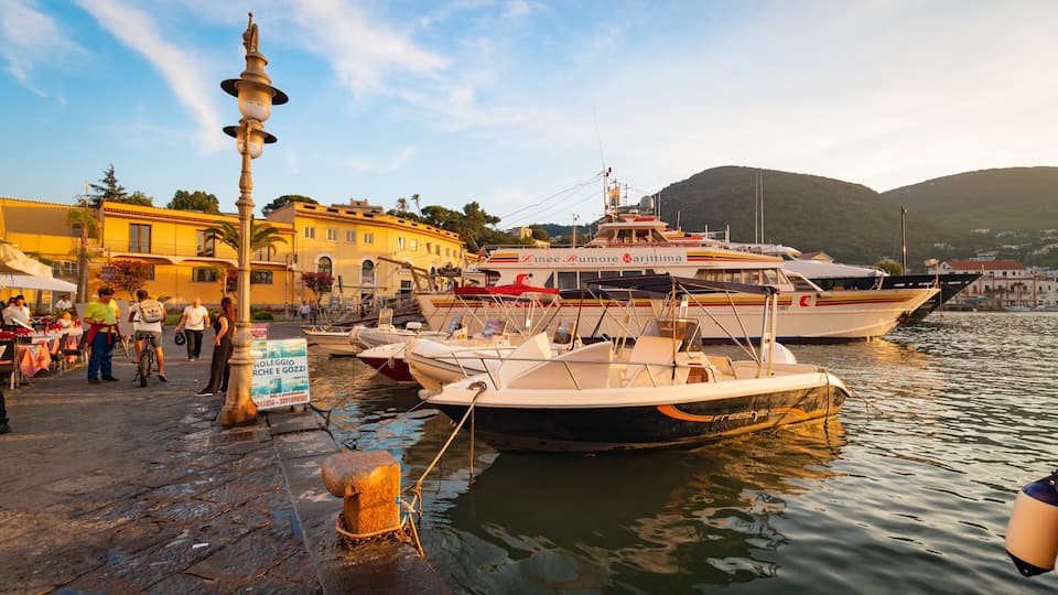 A harbor with boats docked, a street with people, and buildings in the background.