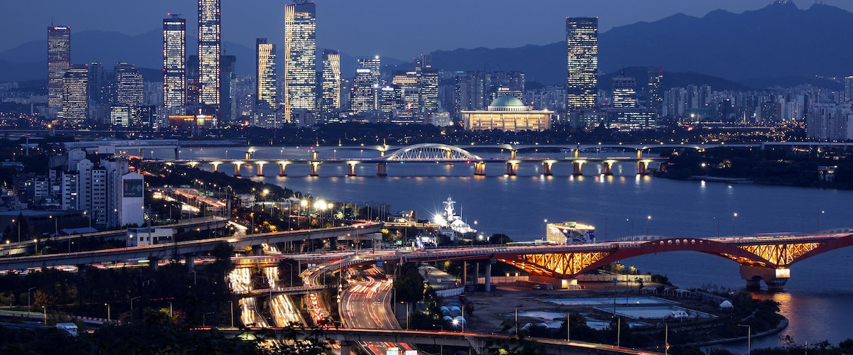 A city skyline at dusk with illuminated buildings, a river, and multiple bridges.