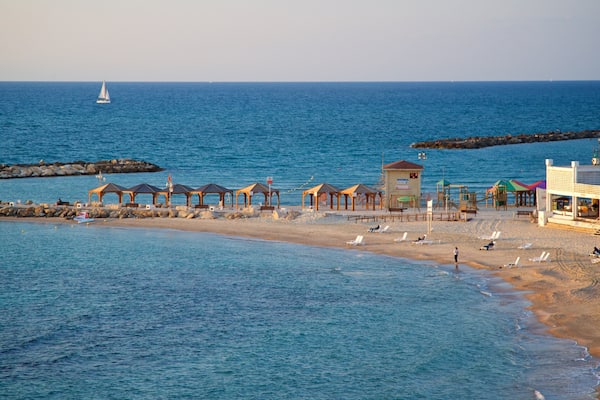 A beach with wooden gazebos, a lifeguard tower, and a rocky breakwater.