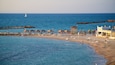 A beach with wooden gazebos, a lifeguard tower, and a rocky breakwater.