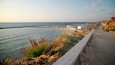 A coastal road with a beach, a lighthouse, and a rocky cliff.