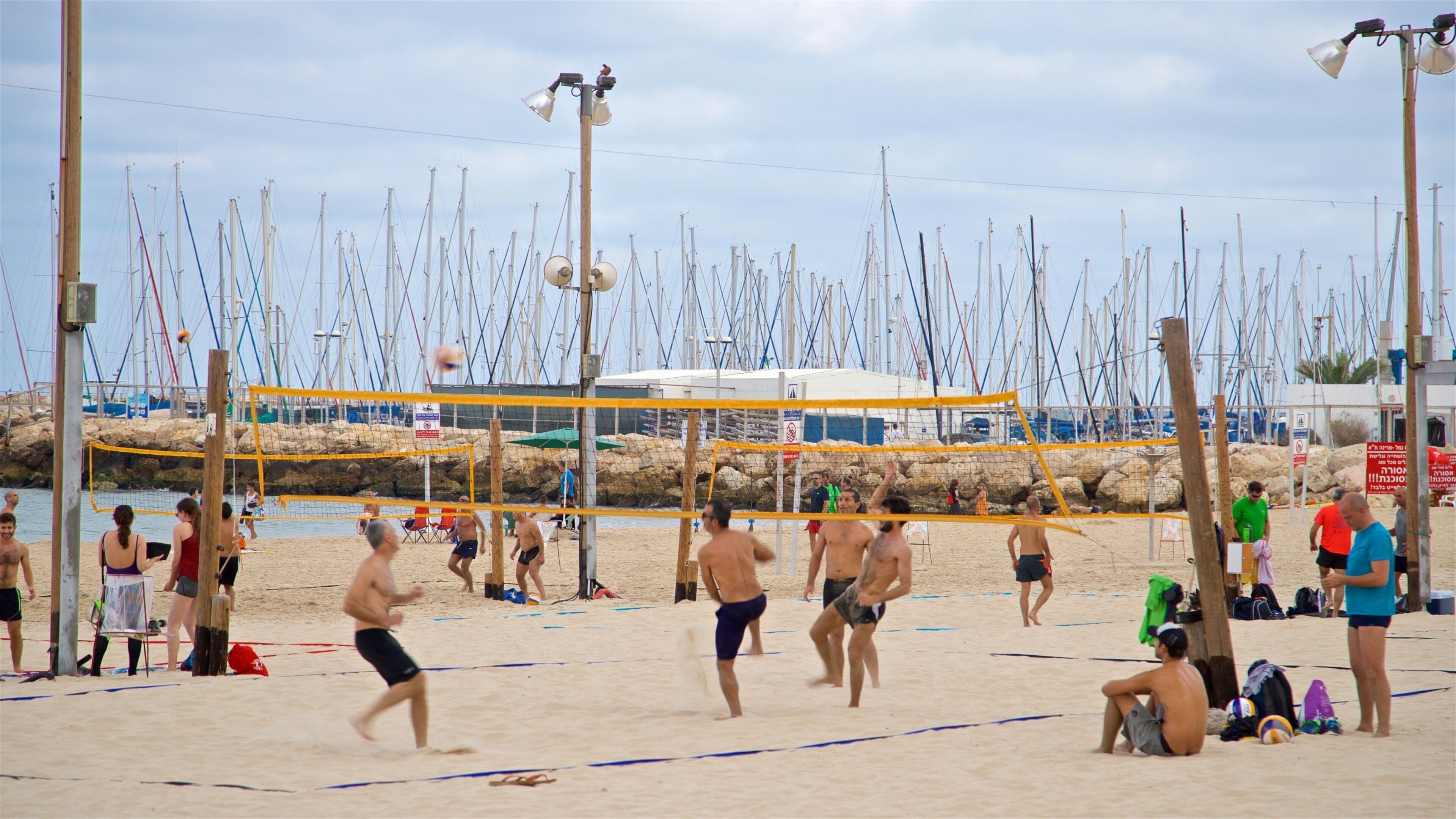 Un match de volleyball de plage avec des joueurs, un filet de volleyball et, en arrière-plan, des bateaux.