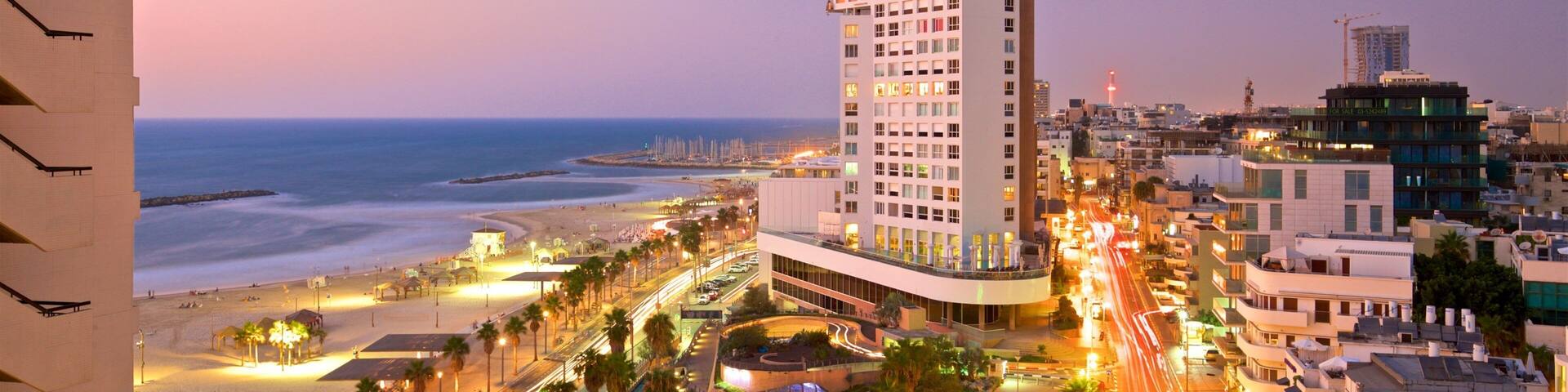 A coastal cityscape with a prominent hotel, beach, and urban streets at dusk.