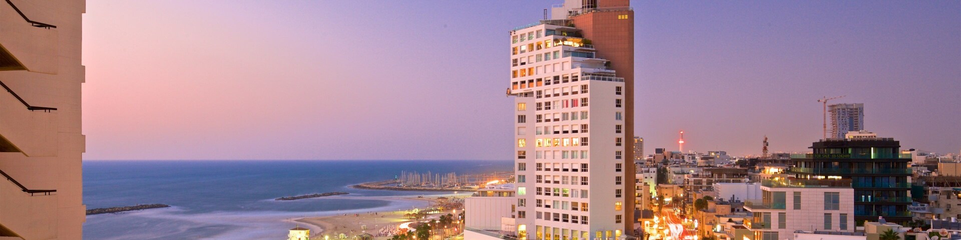 A coastal cityscape with a prominent hotel, beach, and urban streets at dusk.