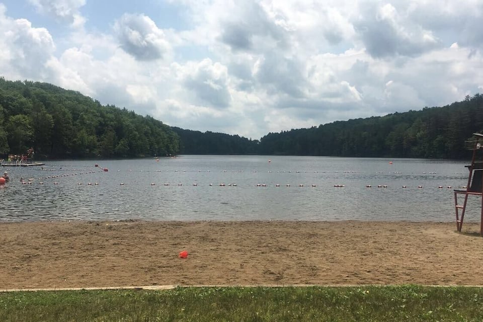 A lake with a beach chair and a 'BEACH CLOSED' sign, surrounded by forested hills.