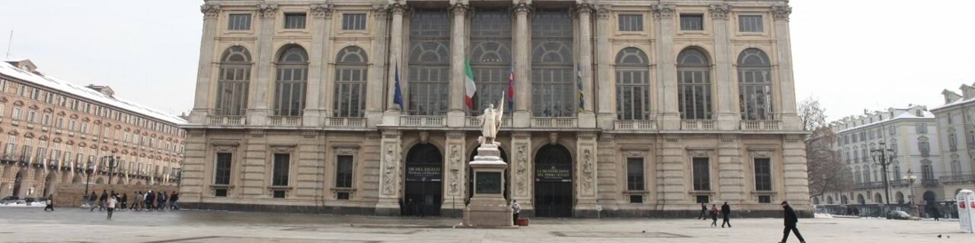 A grand historic building with a central statue, large windows, and flags.