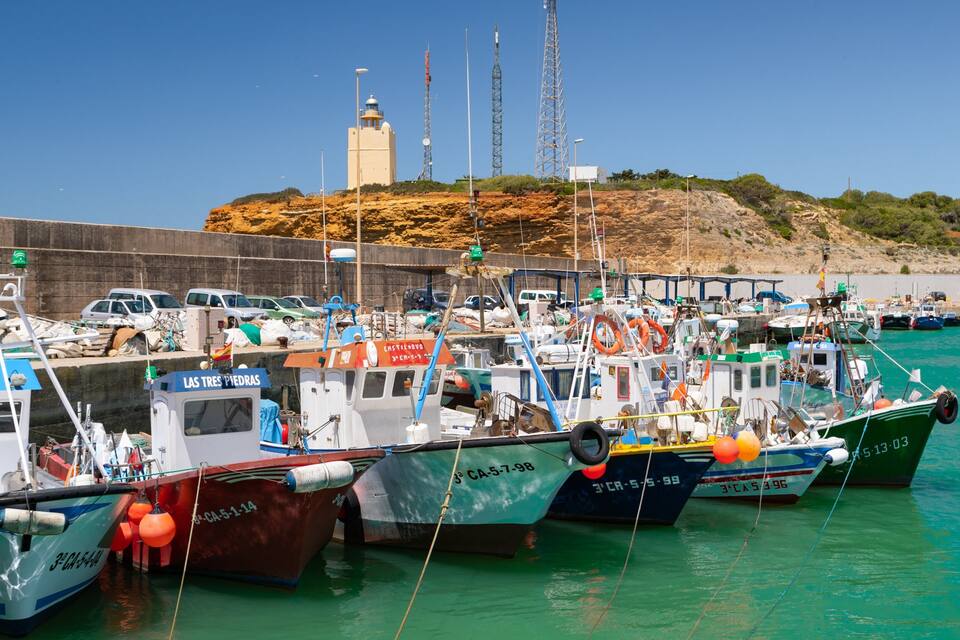 Ein Yachthafen mit mehreren angemeldeten Booten, ein Leuchtturm im Hintergrund und ein felsiger Hügel.