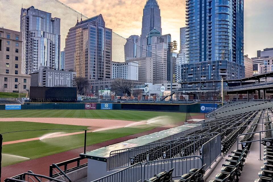 A baseball stadium with empty seats, a baseball diamond, and a city skyline in the background.