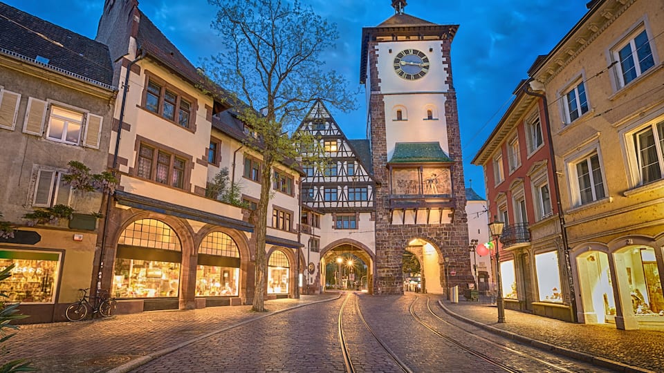 A cobblestone street leading to a historic building with a clock tower, surrounded by traditional European architecture.