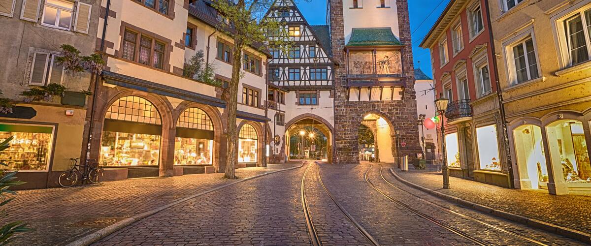 A cobblestone street leading to a historic building with a clock tower, surrounded by traditional European architecture.