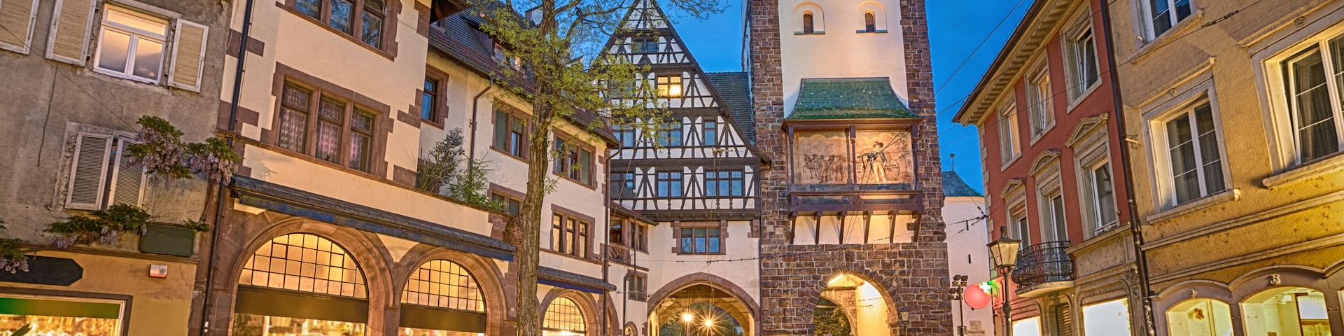 A cobblestone street leading to a historic building with a clock tower, surrounded by traditional European architecture.