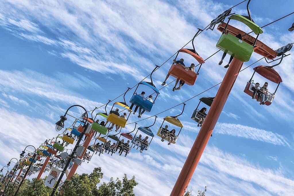 A cable car system with multiple colorful gondolas against a blue sky with clouds.