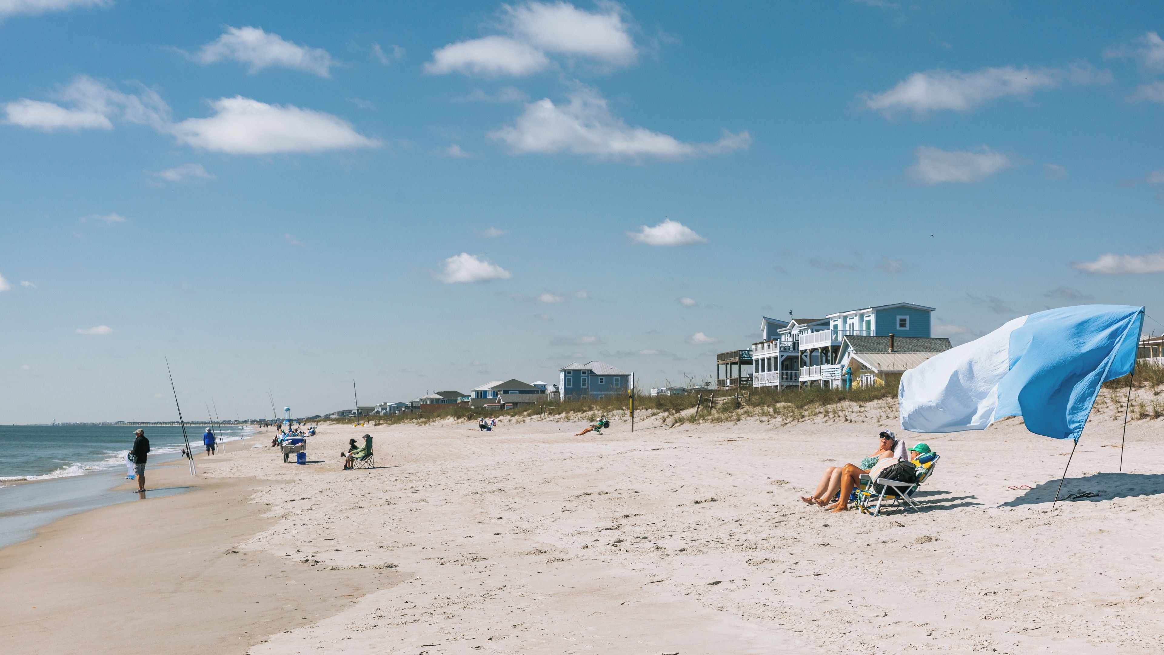 A beach with people fishing, a large house, and a flag.