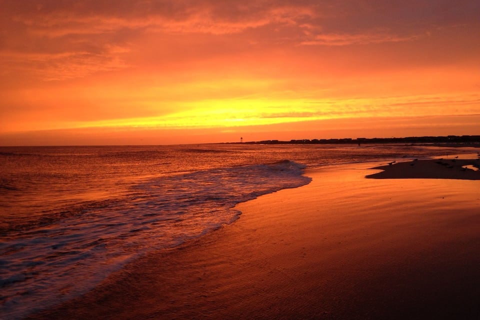 A sunset over a beach with waves gently lapping the shore.