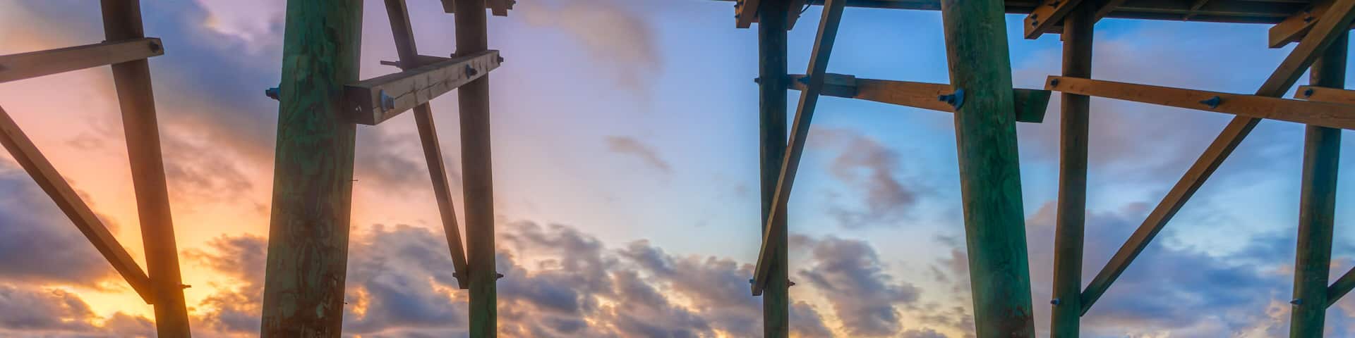 A wooden pier structure over a beach with a sunset in the background.