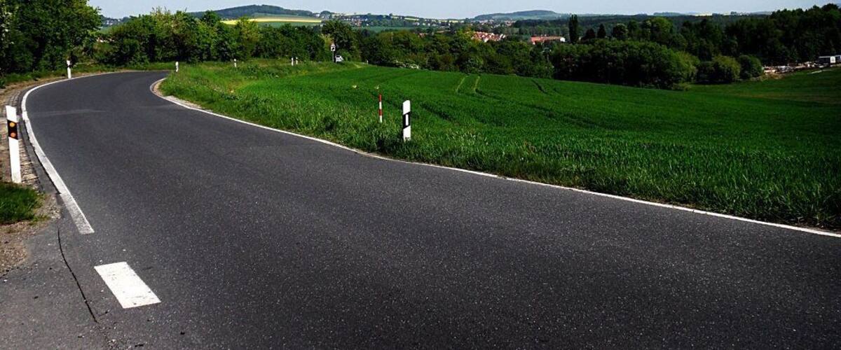 A curving road with green fields and distant hills.