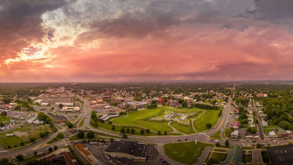 An aerial view of a town with a large green park, a roundabout, and a river.