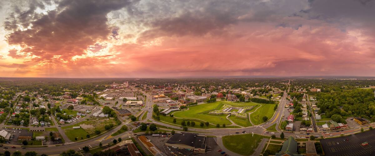 An aerial view of a town with a large green park, a roundabout, and a river.