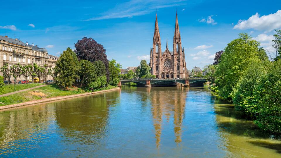 A cathedral with twin spires, a bridge over a river, and surrounding greenery.