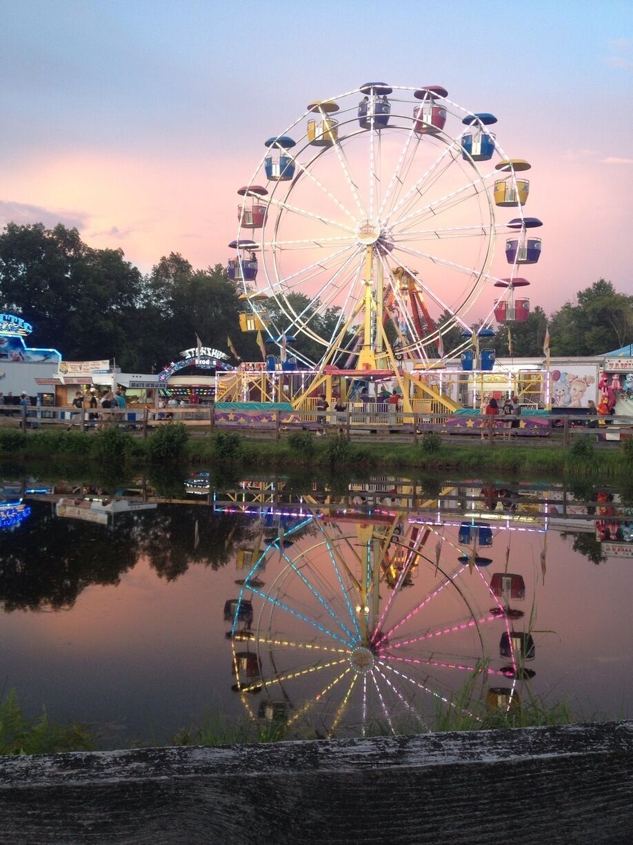 A Ferris wheel at dusk with its reflection in the water.