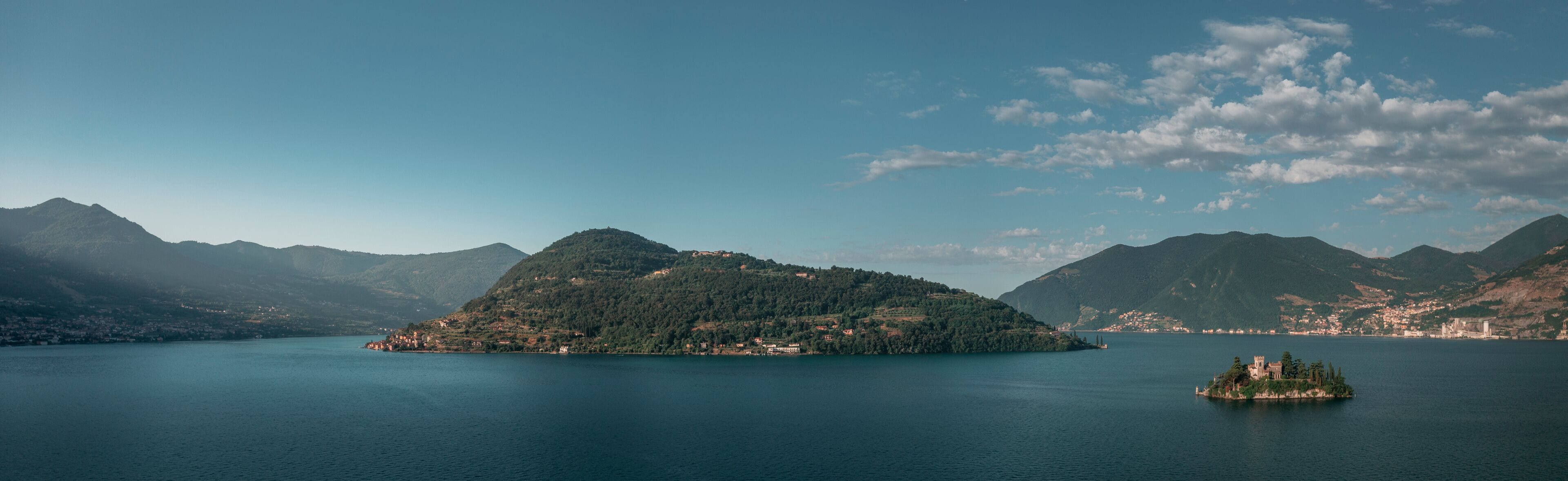 Mountain panorama at Lake Iseo with island Isola di Loreto and Monte Isola from above during afternoon, blue sky, Italy.