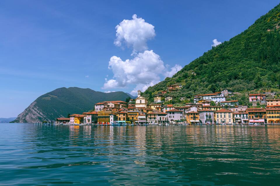 A coastal town with colorful buildings, a church, and a mountain in the background.