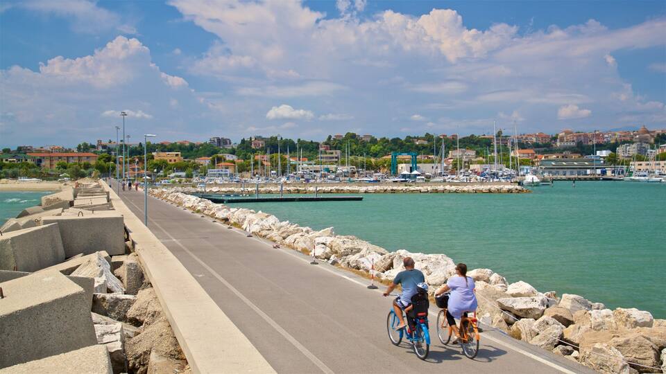A coastal road with cyclists, a marina, and buildings in the background.