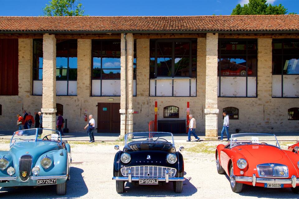 Des voitures anciennes sont garées devant un bâtiment doté de grandes fenêtres et d’un toit recouvert de tuiles.
