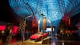A red sports car on display under a glass dome with a checkered flag and a 'Find Your Drive' sign.